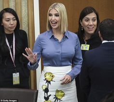 a woman in a blue shirt and white skirt talking to two other women at a conference