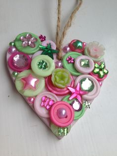 a heart shaped ornament made out of buttons and other decorative items on a white surface