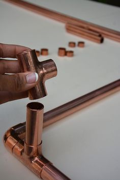 a person holding a metal object in front of some copper pipes on a white surface