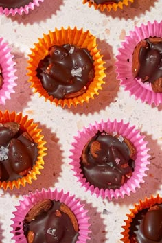 chocolates in pink and orange paper lined up on a white counter top with one bite taken out