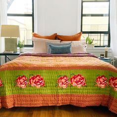 a bed with orange and green bedspread in a bedroom next to two windows