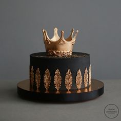 a black and gold cake with a crown on top is shown in front of a gray background