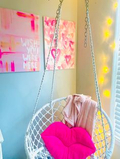 a white hanging chair with pink pillows on it in front of a painting and window