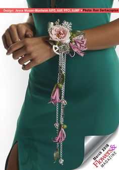 a woman wearing a green dress holding a pink flower and chain bracelet with flowers attached to it