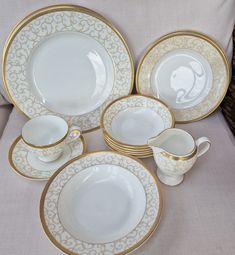 a table topped with lots of white and gold plates covered in fancy design dishes on top of each other