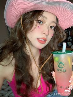 a woman in a pink hat is holding a drink and looking at the camera while wearing a straw hat