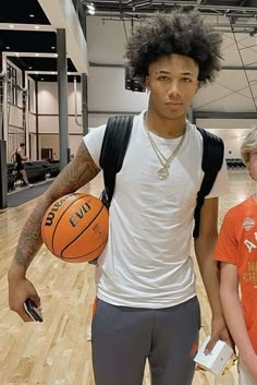 two young men holding basketballs in an indoor gym with hard wood floors and white walls