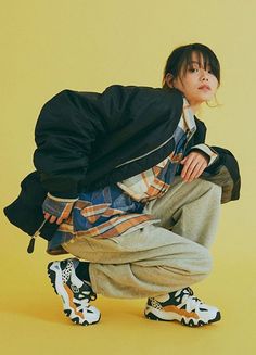 a young man crouching down in front of a yellow background wearing black and white sneakers