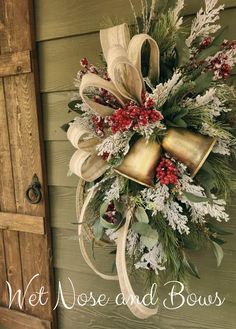 a christmas wreath hanging on the side of a building with bells and evergreens attached to it