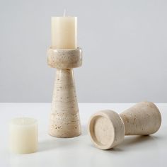 two candles and one candle holder sitting on a table next to each other with white speckles