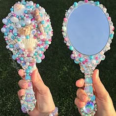 two hands holding up a mirror with seashells and pearls on it in front of a black background