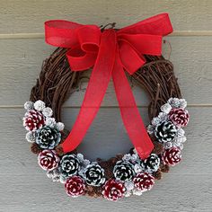 a wreath with pine cones and red ribbon