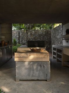 an outdoor kitchen with concrete counter tops and stone walls, along with a television on the wall