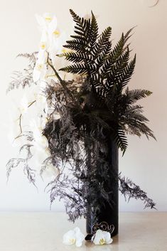 a black vase filled with white flowers and ferns