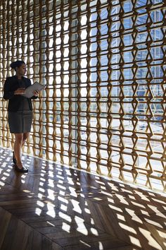 a woman standing in front of a wall made out of wooden slatted panels