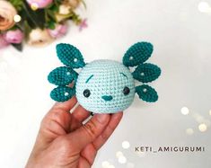 a hand holding a small crocheted stuffed animal with leaves on it's head