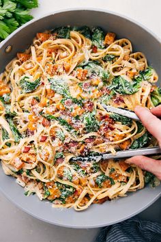 someone is holding a fork in a bowl of pasta with spinach and bacon on it