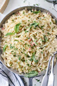 a pan filled with pasta and garnished with parsley on the side next to two silver spoons