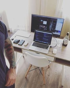 a man sitting in front of a laptop computer on top of a wooden desk next to a white chair