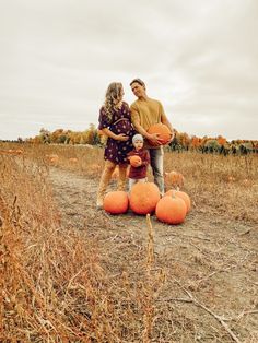 a man and woman standing in a field with pumpkins