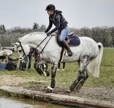 a woman riding on the back of a white horse next to a body of water