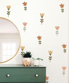 a dresser with a mirror on top of it and flowers painted on the wall behind it