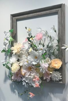 an arrangement of flowers is displayed in front of a framed painting on the wall,