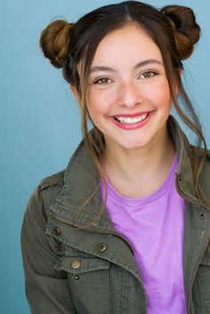 a young woman smiling with her hair in a topknott and wearing a green jacket