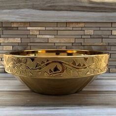 a golden bowl sitting on top of a wooden table next to a brick wall and floor