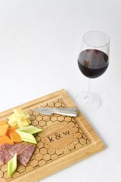 a wooden cutting board with cheese and meat on it next to a glass of wine