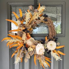 a wreath on the front door with flowers and leaves hanging from it's side