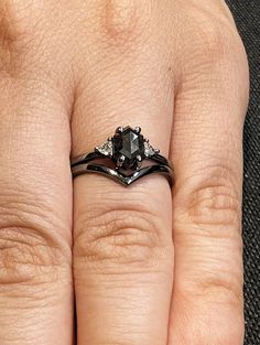 a woman's hand with two black rings on it and an engagement ring in the middle