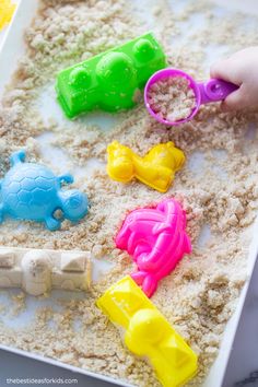 a child is playing with sand and plastic toys in the shape of animals on a white tray