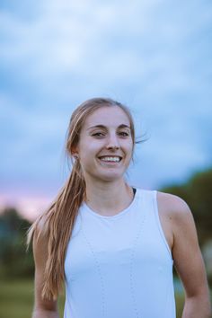 a woman with long hair smiling at the camera while wearing a white tank top and black shorts