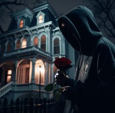 a hooded person holding a rose in front of a house