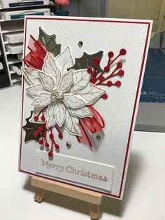 a christmas card on a easel with red and white paper, poinsettis and holly