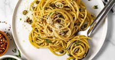 a white plate topped with pasta and sauce next to two small bowls filled with pesto