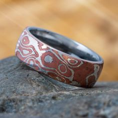 This titanium ring features a copper and silver mokume gane overlay. Mokume-gane is a mixed-metal laminate with distinctive layered patterns. Translated as wood-grain metal, the name was borrowed from a pattern created in the forging of Samurai swords and other sharp-edged tools.The traditional components were relatively soft metallic elements and alloys such as gold, copper, silver, shakudo, shibuichi, and kuromido. After the original metal sheets were stacked and carefully heated, the solid bi Mokume Gane Ring, Damascus Ring, Unique Mens Rings, Metal Sheets, Titanium Jewelry, Mokume Gane, Titanium Ring, Samurai Swords, Unique Wedding Bands