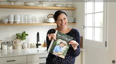 a woman standing in a kitchen holding up a cookbook