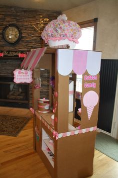 a cardboard ice cream parlor with pink and white decorations on the top, in front of a fireplace