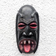 a black mask with red eyes and teeth on a white wall, showing its mouth wide open