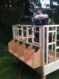 a man standing on top of a wooden structure in the middle of a yard with a hose attached to it