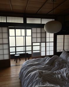 an unmade bed in a room with large windows and wooden flooring on the side