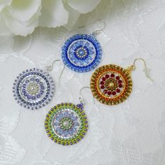 three different colored earrings sitting on top of a white table next to a bouquet of flowers