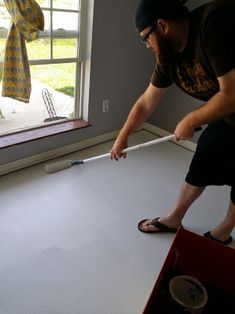 a man standing on top of a white floor in front of a window next to a red box