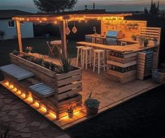 an outdoor kitchen with lights on the roof and bar stools in the back yard