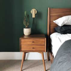 a nightstand with a potted plant on it next to a bed in a bedroom