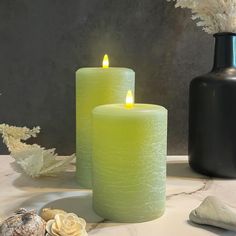 two green candles sitting on top of a table next to shells and flowers in vases