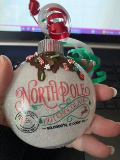 someone holding a christmas ornament in front of a laptop computer with the words north pole hot chocolate on it