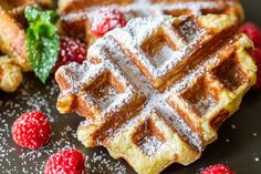 waffles with powdered sugar and raspberries on a black plate, ready to be eaten